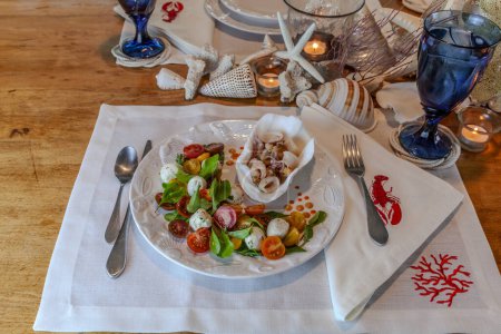 Mezcla de mariscos y ensalada Caprese con tomates cherry, mozzarella, albahaca y rúcula en un bonito plato con una mesa de decoración de concha marina.