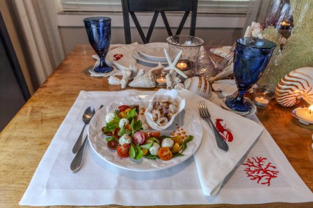 Mezcla de mariscos y ensalada Caprese con tomates cherry, mozzarella, albahaca y rúcula en un bonito plato con una mesa de decoración de concha marina.