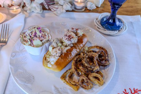 Lobster salad in a fresh brioche roll with homemade fried onion rings and coleslaw and a glass of cold lemonade. 