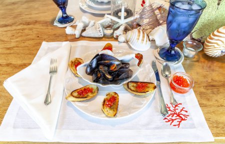 Clamshell dish of mussels and garlic with red wild salmon caviar roe on pesto French bread in a nautical setting.