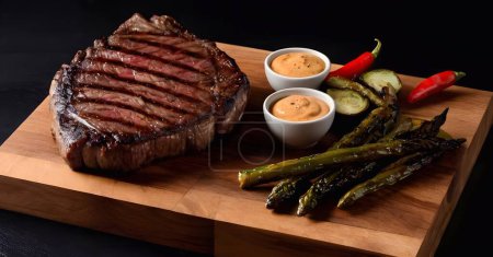 steaks de filet mignon avec des marques de gril parfaites sont présentés sur une planche à découper en bois, accompagné d'asperges, et les carottes, mettant en valeur un bien préparé.