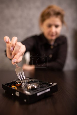 Téléchargez les photos : A business woman scrapes a hard disk with data with a fork - en image libre de droit