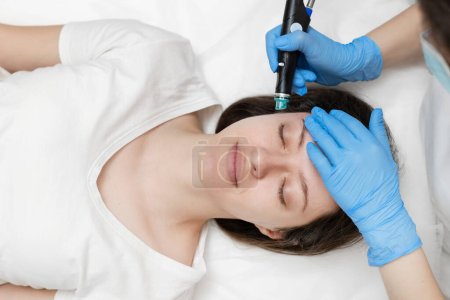 Cosmetólogo experto inteligente usando un dispositivo moderno mientras hace el procedimiento hidrafacial