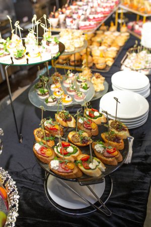 Catering buffet table with delicious appetizers and snacks for guests at a party or corporate event. Decorated with black tablecloth and napkins, food arranged visually.