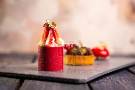 Tarte au chocolat, mousse de fraise, macaron de framboise sur panneau d'ardoise avec fond rose pour un élégant dessert.