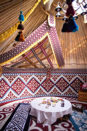 Interior of a Central Asian yurt with felt carpets, furniture, and a table. Traditional nomadic dwelling with white tablecloth.