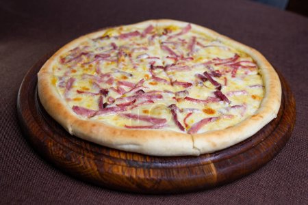 Savory pizza topped with gooey melted cheese and sliced ham, shot in a well-lit setting with a blurred background, creating an appetizing image.