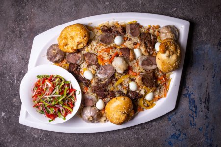 Foto de Imagen de riego bucal del plato Plov uzbeko con cordero, arroz, zanahorias, cebollas y especias en el plato blanco. Fondo rústico añade autenticidad. - Imagen libre de derechos