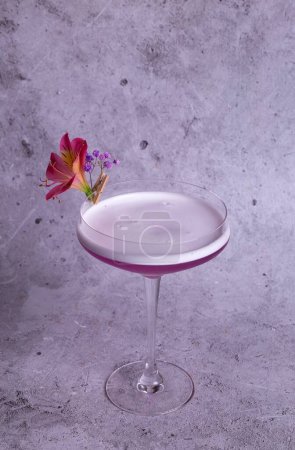 Image élégante d'un cocktail rose dans un verre avec une garniture de fleurs sur un fond gris, exsudant classe et sophistication.