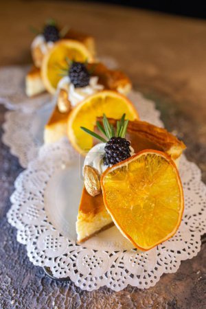 Eine dekadente Präsentation von vier Scheiben cremigem Käsekuchen mit leuchtenden Orangenscheiben und saftigen Brombeeren auf einem zierlichen weißen Deckchen.