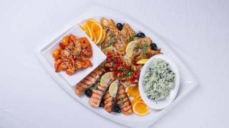 top view of a delicious seafood and rice dish on a white platter with an orange side dish.