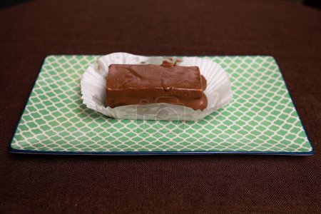 This image shows a piece of homemade chocolate fudge resting on a white paper wrapper on a light green textured background.