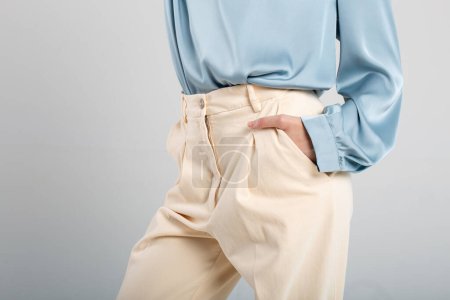 Modemodel in beiger Hose und blauer Bluse mit Hand in Tasche auf isoliertem Hintergrund. Geeignet für Mode-Anzeigen.