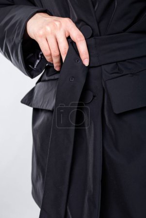 A woman adjusts the belt of a black blazer with slim fit and classic collar, creating a chic and sophisticated business attire look.