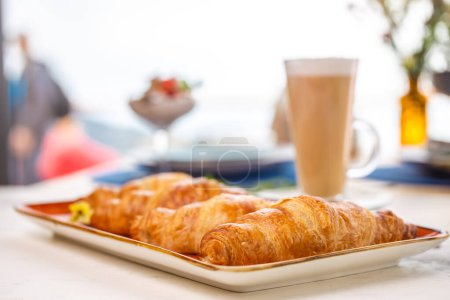 Photo for A delightful breakfast with croissants and coffee on a marble table. Croissants are golden brown on an orange plate, coffee with froth. - Royalty Free Image