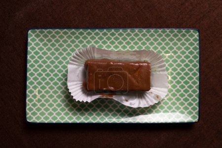 Esta imagen muestra un trozo de dulce de chocolate casero descansando sobre una envoltura de papel blanco sobre un fondo de textura verde claro.