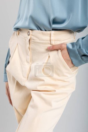 Modemodel in beiger Hose und blauer Bluse mit Hand in Tasche auf isoliertem Hintergrund. Geeignet für Mode-Anzeigen.