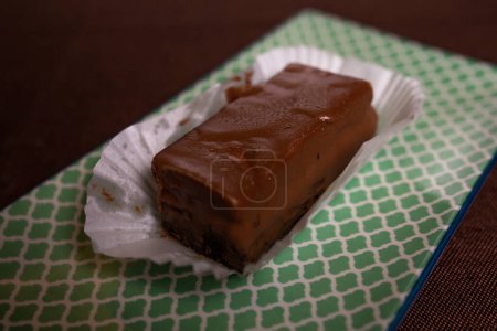 This image shows a piece of homemade chocolate fudge resting on a white paper wrapper on a light green textured background.
