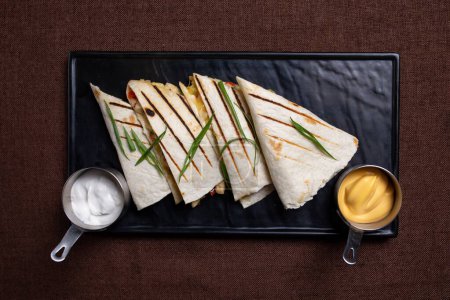 A flavorful quesadilla loaded with chicken, cheese, veggies, sour cream, and salsa, perfect for any mealtime or celebration.