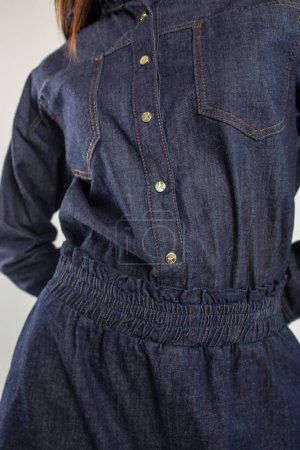 Foto de Una mujer joven en un vestido de mezclilla azul con cuello y mangas largas. Ajustado en la cintura con una cintura elástica. - Imagen libre de derechos