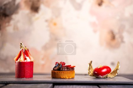 Indulgent chocolate tart, strawberry mousse, raspberry macaroon on slate board with pink background for an elegant dessert display.