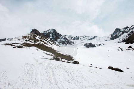 Un paisaje invernal de montañas cubiertas de nieve y colinas con una cumbre rocosa en la distancia y colinas cubiertas de nieve en primer plano, tomadas en un día brillante con un cielo azul y nubes blancas.
