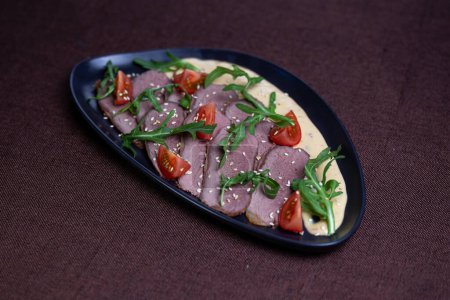 Savor the succulent flavors of pan-seared duck breast served with a vibrant arugula salad topped with cherry tomatoes, sprinkled with toasted sesame seeds, and drizzled with a luscious creamy sauce.