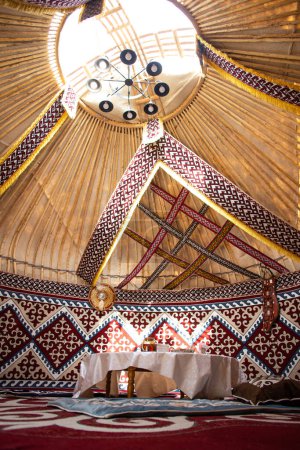 Interior de una yurta de kazak con alfombras de fieltro, muebles y una mesa. Vivienda nómada tradicional con mantel blanco.