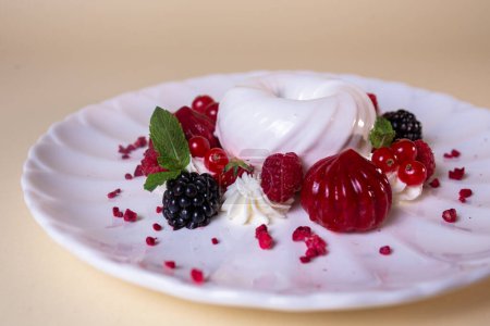 Decadent cake with cream, strawberries, blueberries, raspberries on white plate, isolated on beige background.