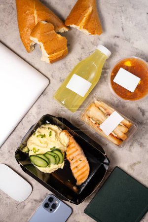 A laptop on a table with a delicious lunch sandwich, salad, and drink. Ideal for work break or business meeting.