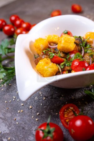 Salat mit gegrilltem Huhn, Tomaten und Zwiebeln auf einer weißen Schüssel mit Dill und Tomaten auf der Seite. Vereinzelt auf schwarzem Hintergrund.