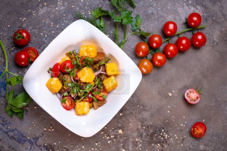 Ensalada con pollo a la parrilla, tomates y cebollas en un tazón blanco con eneldo y tomates en el lado. Aislado sobre un fondo negro.