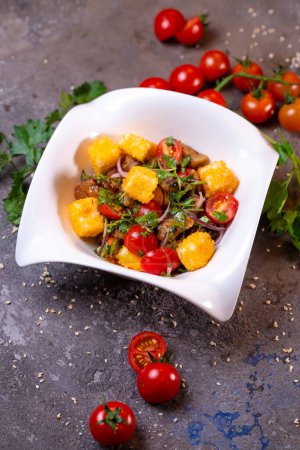 Salat mit gegrilltem Huhn, Tomaten und Zwiebeln auf einer weißen Schüssel mit Dill und Tomaten auf der Seite. Vereinzelt auf schwarzem Hintergrund.