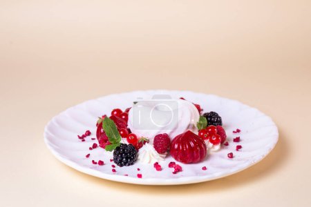 Dekadenter Kuchen mit Sahne, Erdbeeren, Blaubeeren, Himbeeren auf weißem Teller, isoliert auf beigem Hintergrund.