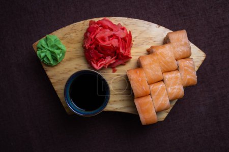 Zbliżenie tradycyjnych japońskich bułek sushi, wasabi pasty i marynowany imbir na drewnianym talerzu na ciemnym tle