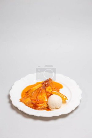 Verwöhnen Sie sich mit einem verführerischen Dessert aus Crêpes, gebadet in einer würzigen Orangensoße und gekrönt mit cremigem Eis für einen köstlichen Genuss.