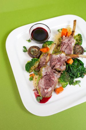 A delicious and healthy rib dish with mushrooms, broccoli, carrots and spinach on a white plate on a green background.