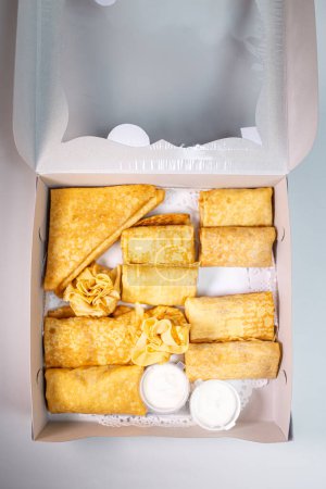 12 panqueques pequeños con rellenos dulces y salados en una caja blanca. Las opciones incluyen queso, papa y carne. Perfecto para el desayuno o merienda.