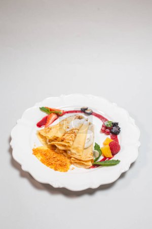 Assiette décadente de crêpes remplies d'une garniture de fromage sucré et crémeux et garnie de fraises fraîches, de bleuets et de groseilles rouges.