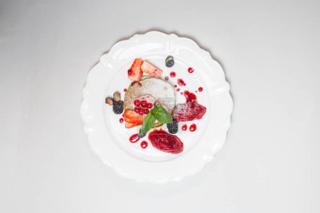 Frische Erdbeeren, Blaubeeren, Preiselbeeren und Brombeeren mit Sahne auf weißem Teller. Gesundes Frühstück und Ernährungskonzept.