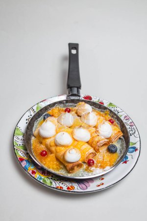 Pancakes with meringue and berries in a frying pan on a white background.