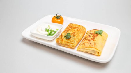 Two folded stuffed savory crepes with sour cream and chives garnish on a white plate on a white background.