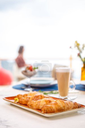 Savor a delectable breakfast spread featuring freshly baked croissants, steaming hot coffee, and a panoramic view from a charming terrace.