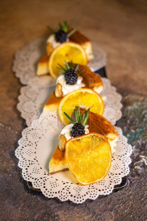 A decadent display of four slices of creamy cheesecake adorned with vibrant orange slices and juicy blackberries on a dainty white doily.