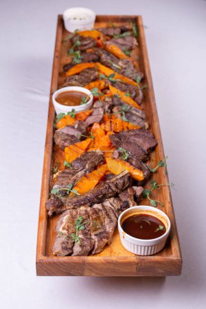 Atrakcyjny asortyment mięs, ziemniaków i sosów pięknie prezentowanych na drewnianej desce na obfity i satysfakcjonujący posiłek.