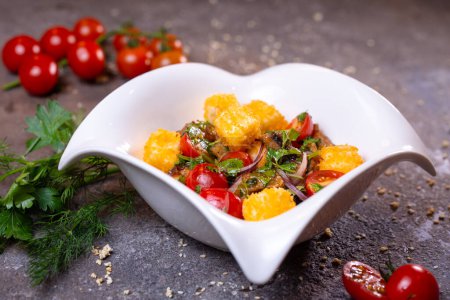 Ensalada con pollo a la parrilla, tomates y cebollas en un tazón blanco con eneldo y tomates en el lado. Aislado sobre un fondo negro.