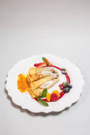A decadent plate of crepes filled with a sweet and creamy cheese filling and topped with fresh strawberries, blueberries, and red currant.