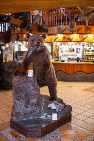 Stuffed brown bear with fish in mouth in cozy lodge with wood walls and fireplace. Wildlife decor theme adds charm to setting.