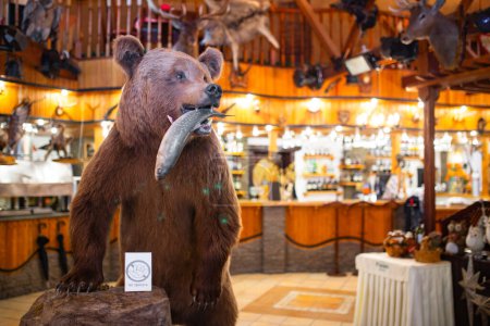 Stuffed brown bear with fish in mouth in cozy lodge with wood walls and fireplace. Wildlife decor theme adds charm to setting.