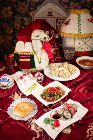 Kasachischer Dastarkhan mit Beshbarmak, Manty, Samsa, Baursak, Jurten-förmigem Zelt, Kamelsattel und traditionelleren Gerichten.